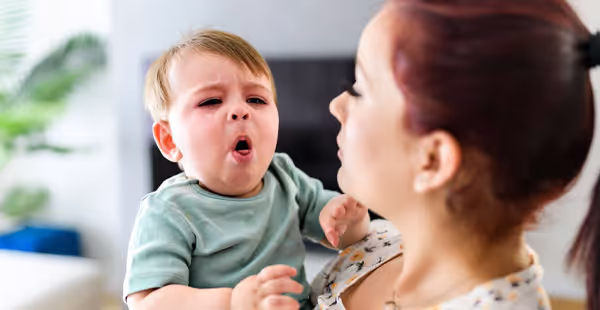 A woman holding a baby with a green shirt.